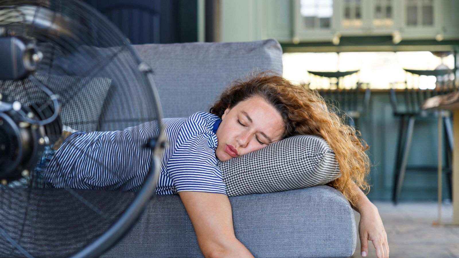Dona jove ficada al llit davant del ventilador elèctric a casa