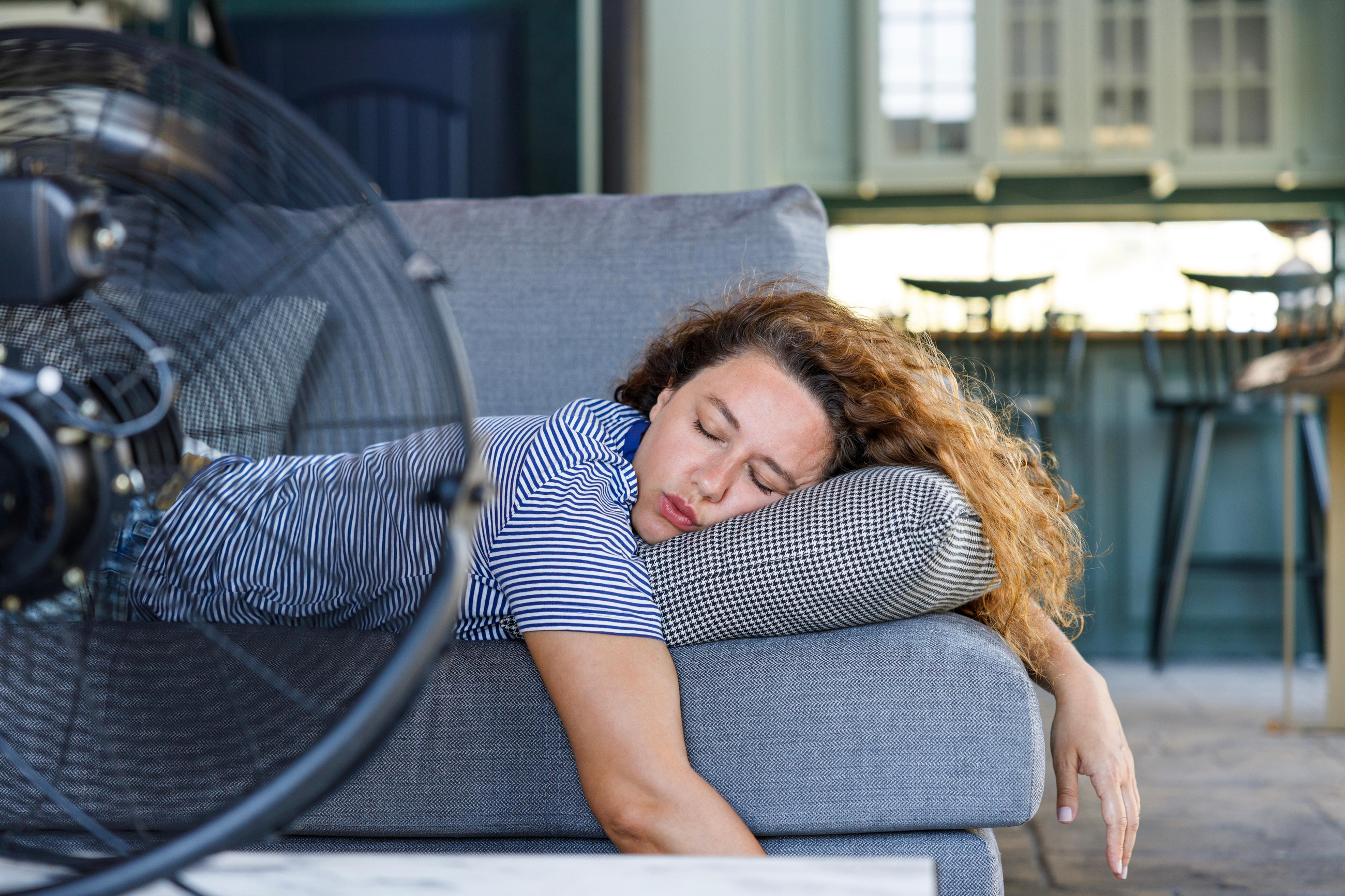 Dona jove ficada al llit davant del ventilador elèctric a casa