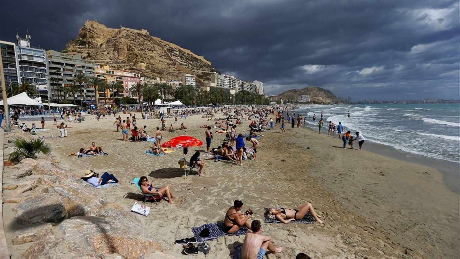 El turistes desafien l'amenaça de pluges a la platja del Postiguet d'Alacant