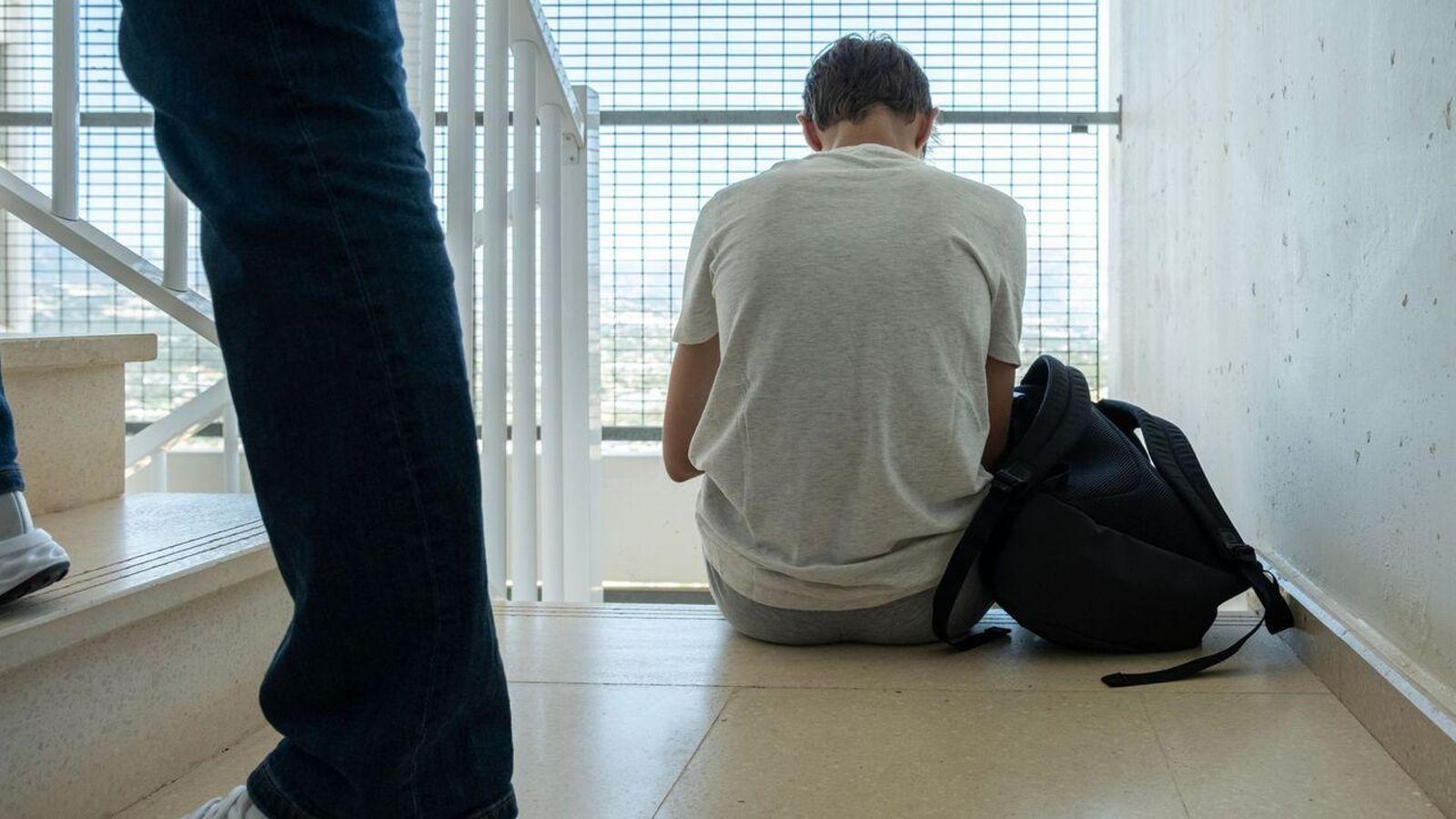 Un adolescent, assegut d'esquenes a l'escala d'un centre educatiu