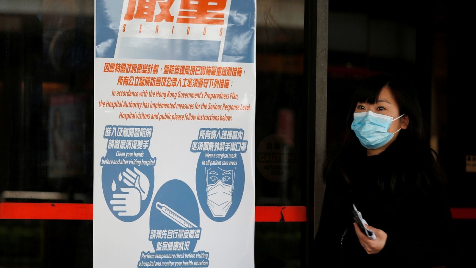 Una dona amb màscara al costat d'un cartell d'advertiment de salut, a Hong Kong, la Xina