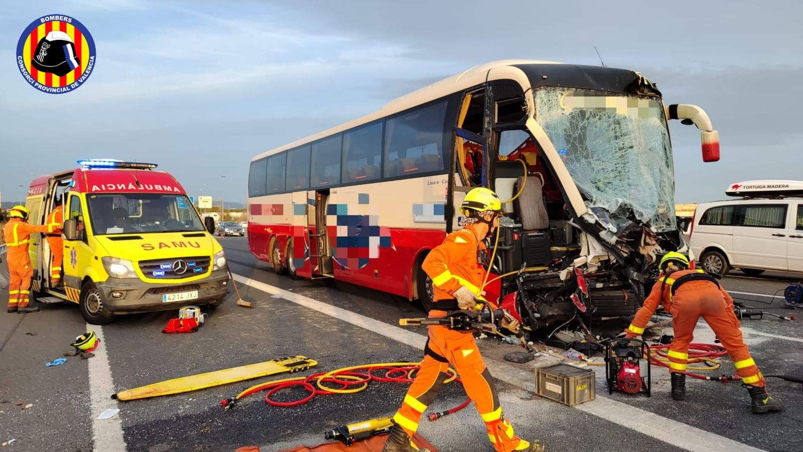 En imatge, l'autobús accidentat al costat d'un SAMU, mentre efectius de bombers netejen la via