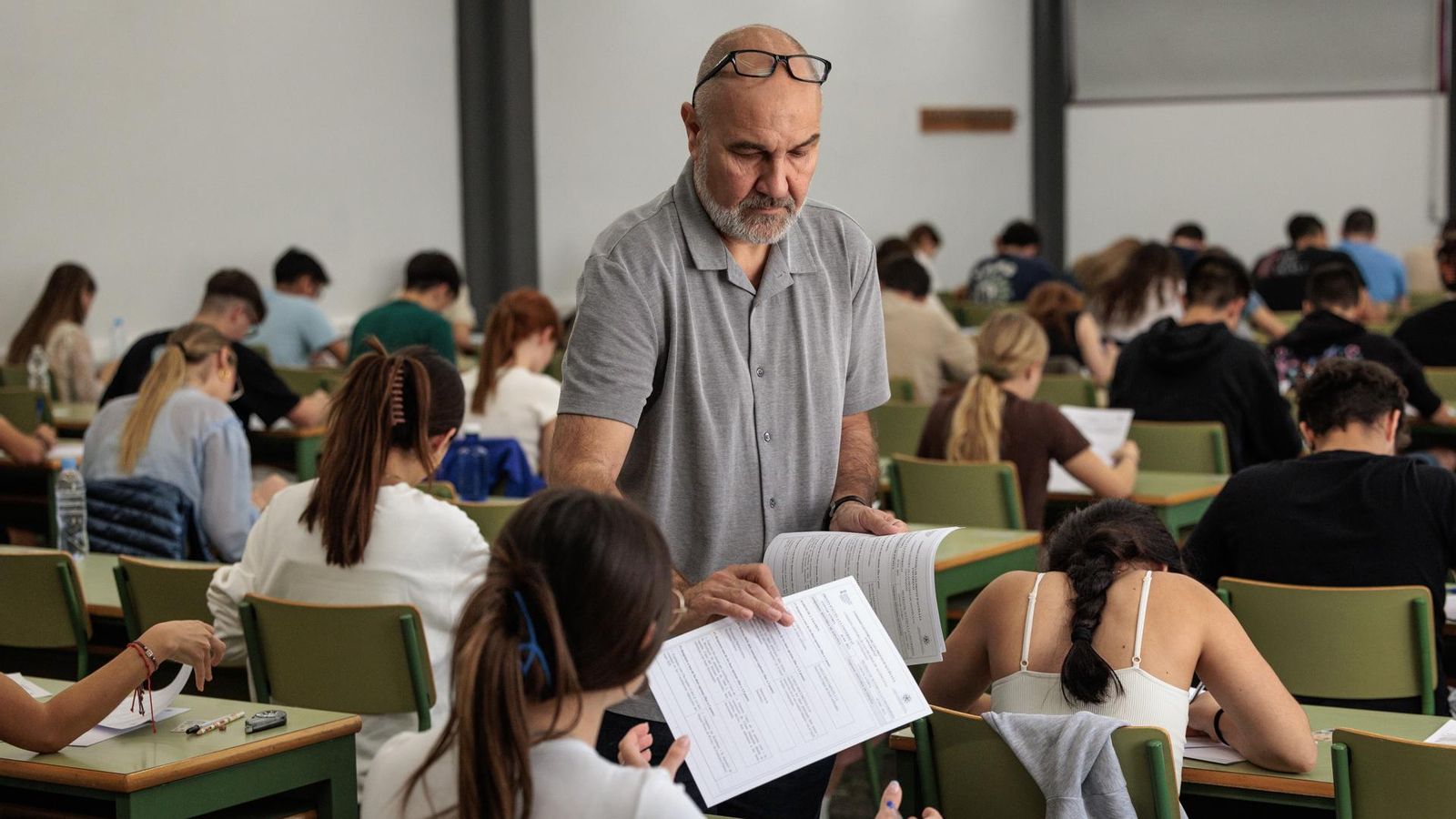 Un examinador reparteix els examens entre l'alumnat en una de les aules en què tenen lloc les PAU