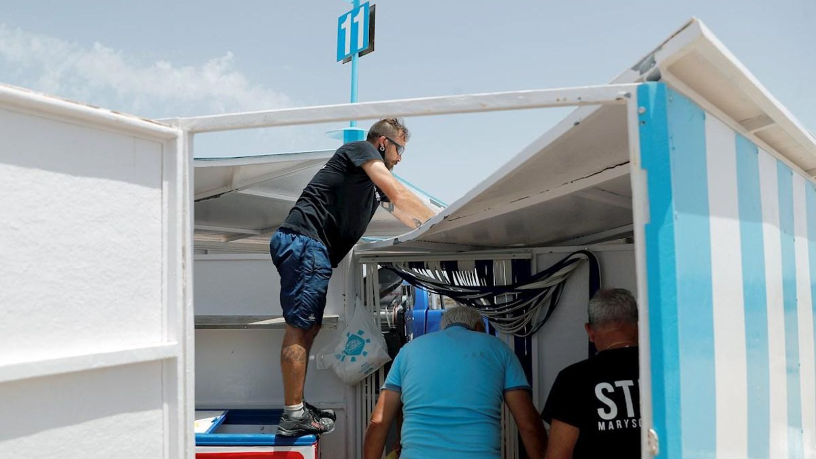 Uns operaris arreglen la teulada d'un quiosquet de la platja de la platja de la Malva-rosa sobre el què botaven els participants d'un dels botellots