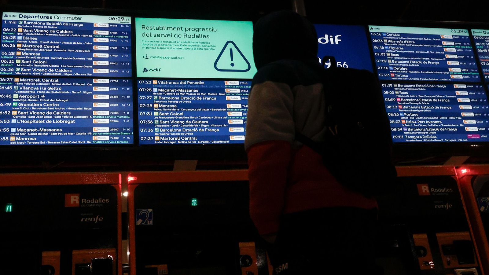 Un viatger observa el panell de l'estació de Sants de Barcelona, on s'informa de la progressiva recuperació del servei de rodalia després de les dos incidències