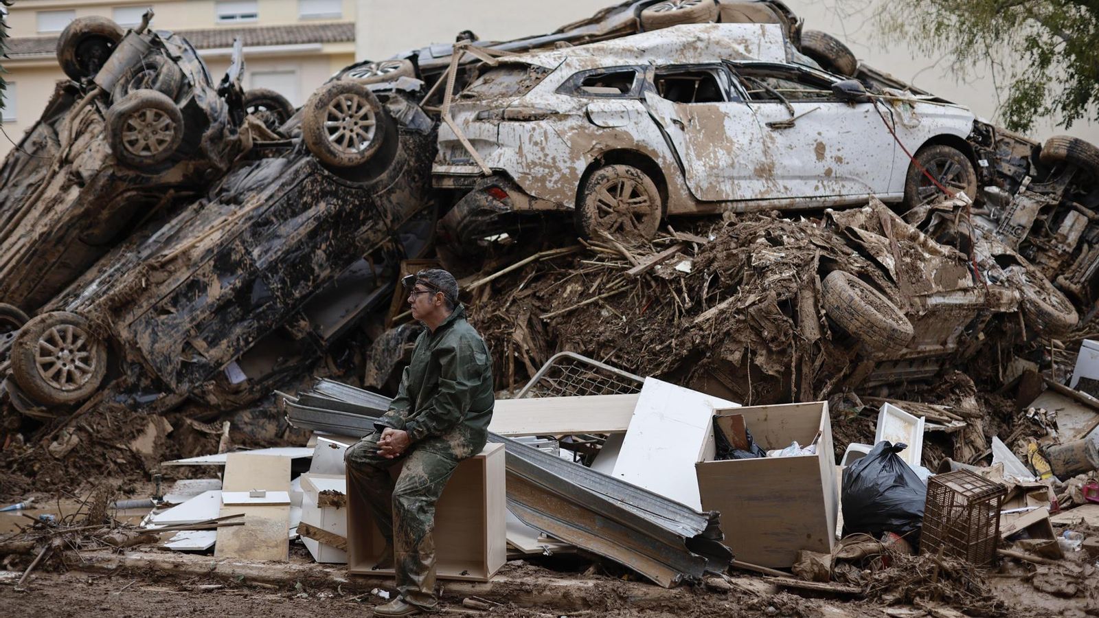Un voluntari descansa assegut al costat d'una muntanya de cotxes a Paiporta (Horta Sud)