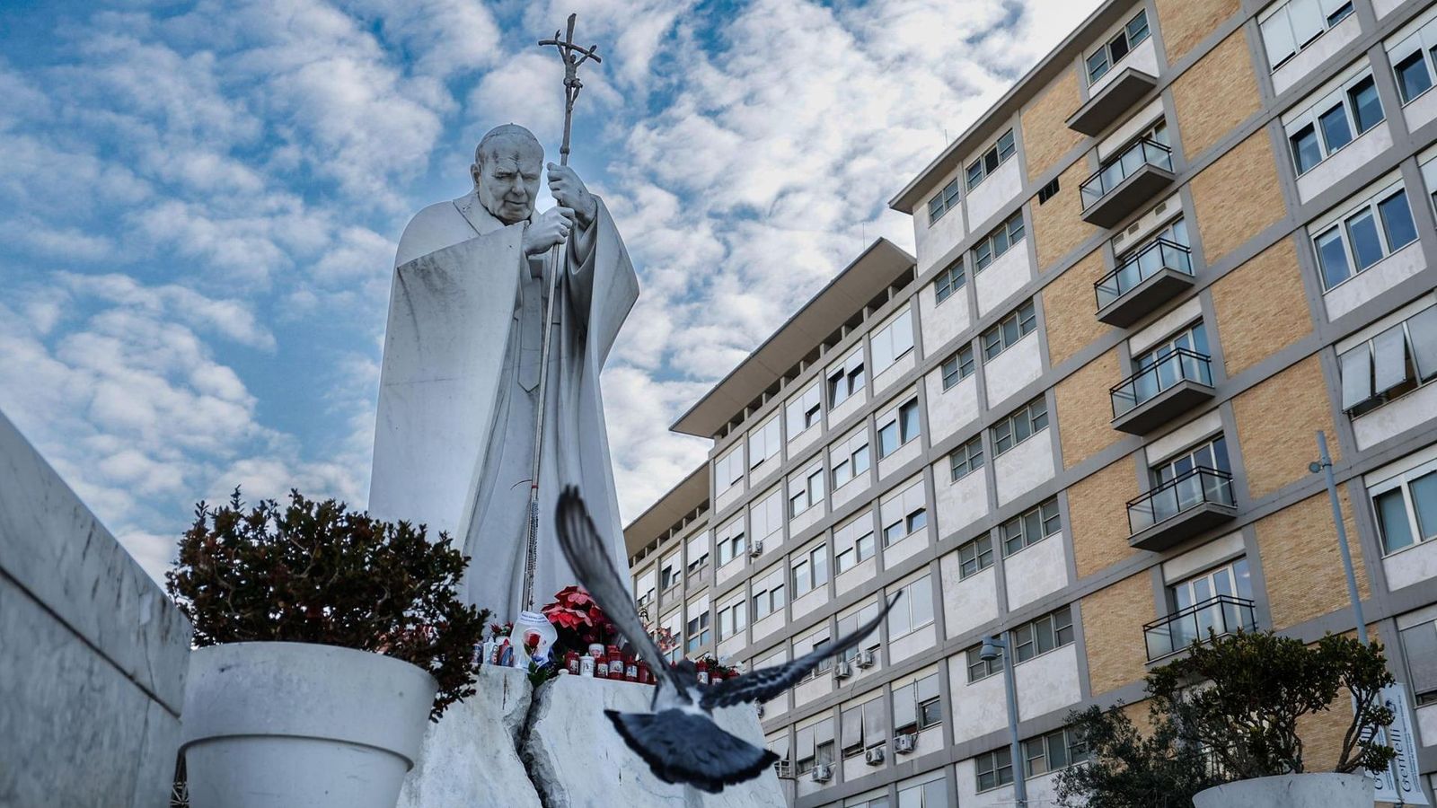 Estàtua del papa Joan Pau II, davant de l’hospital on està ingressat el pontífex Francesc, on els fidels han dipositat flors i ciris