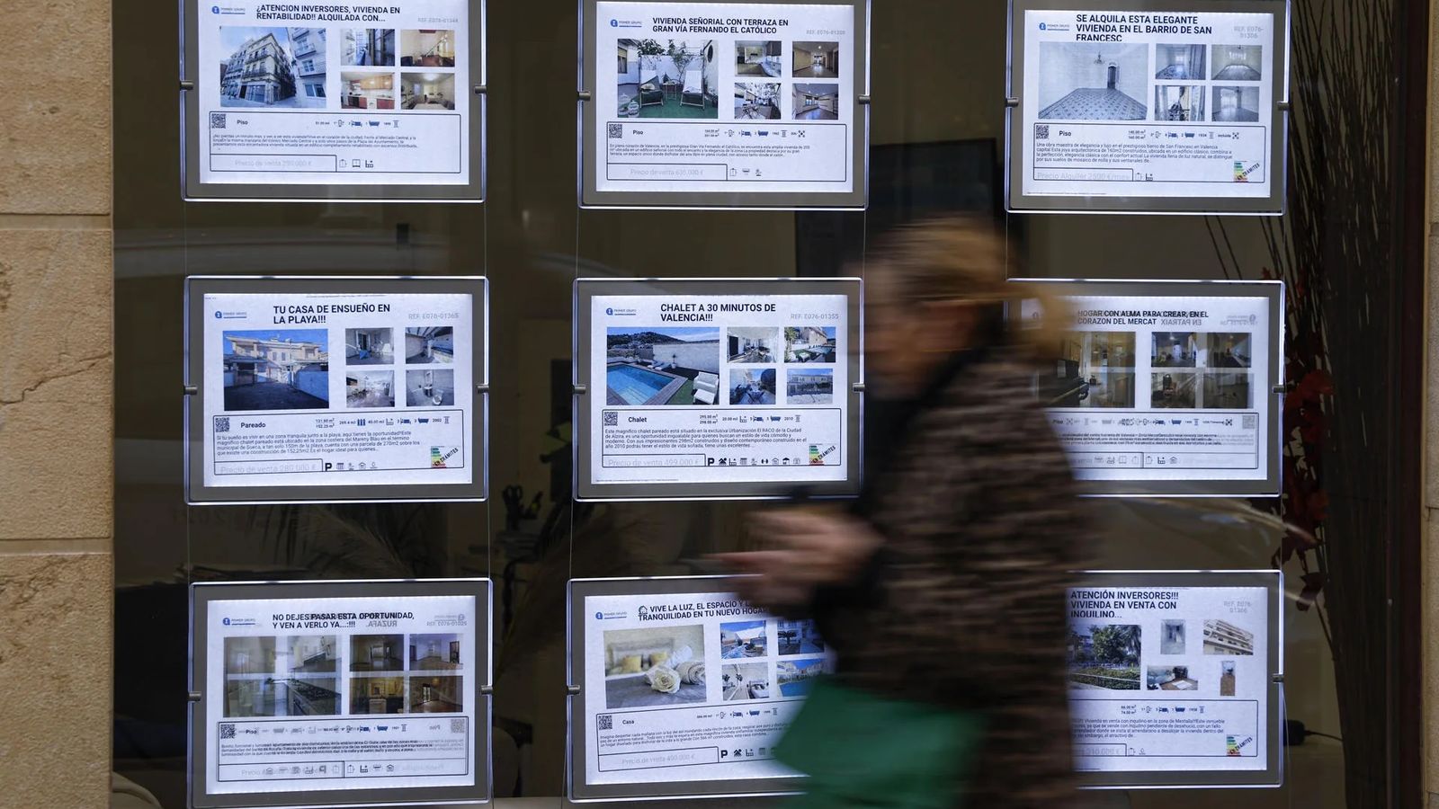 Una dona passa davant els anuncis de venda i lloguer d'habitatge en una immobiliària de València