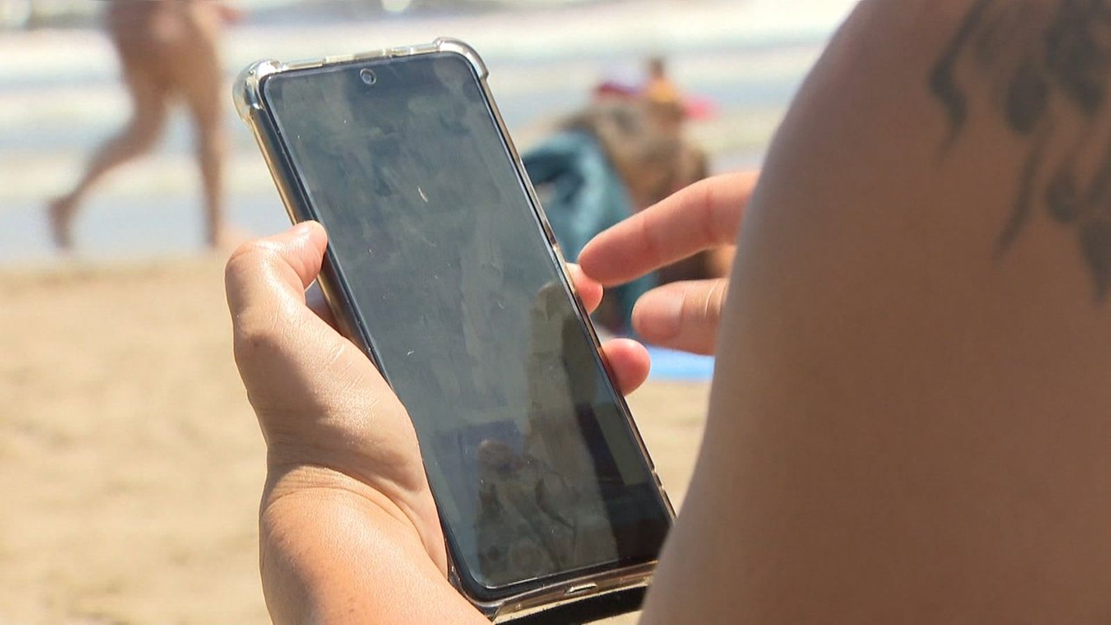 Una persona usa el mòbil mentre està a la vora del mar