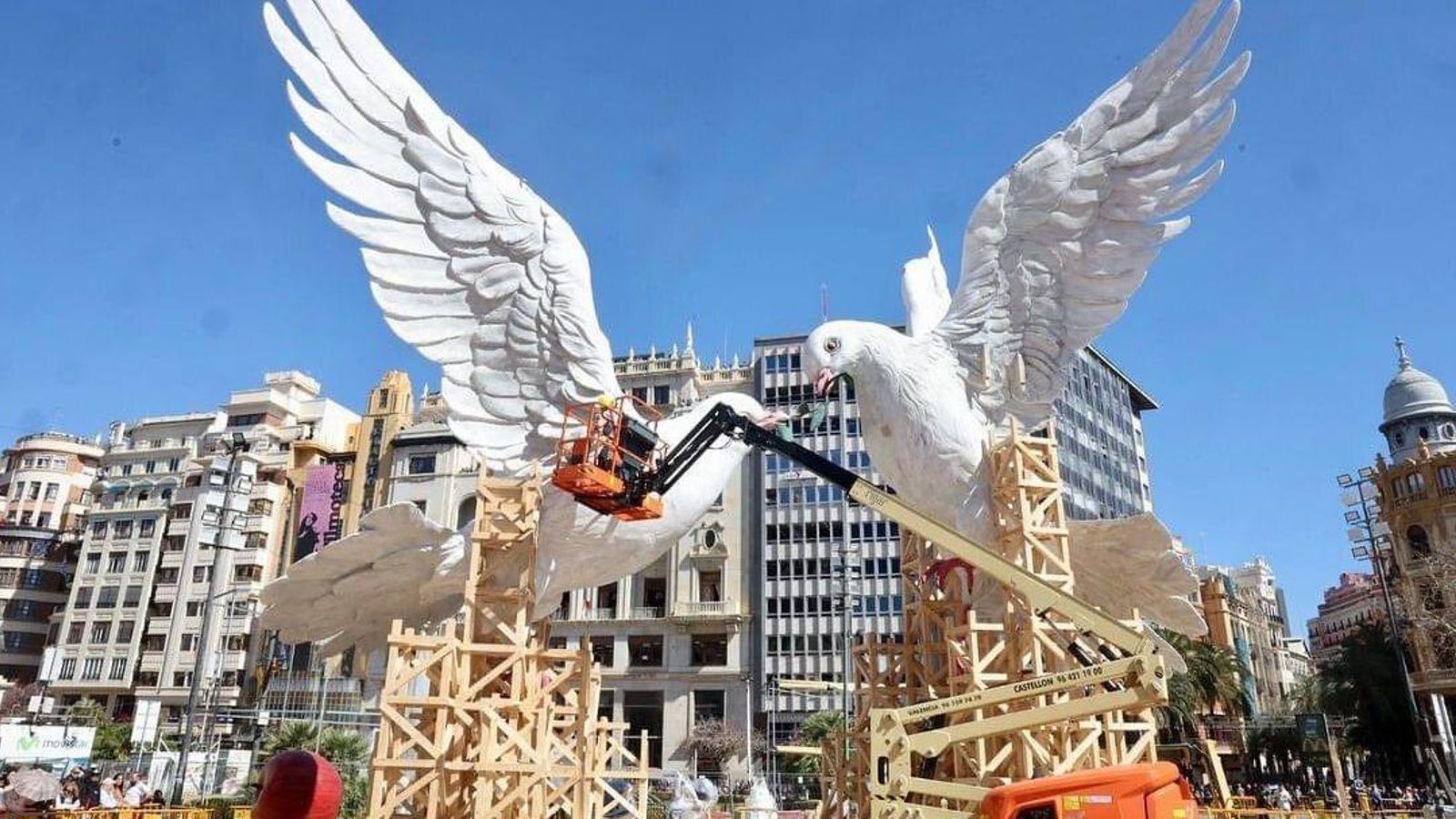 Operaris de l'equip de l'artista de la falla municipal supervisen el muntatge del monument des de la grua