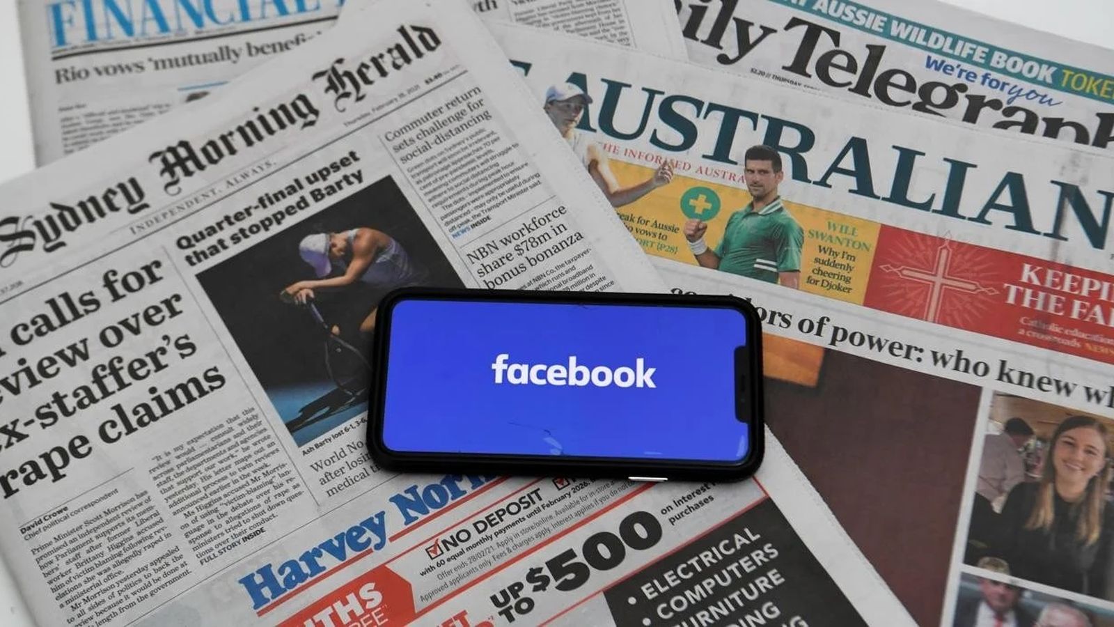 Un movil amb el fons de pantalla de Facebook damunt de periòdics australians