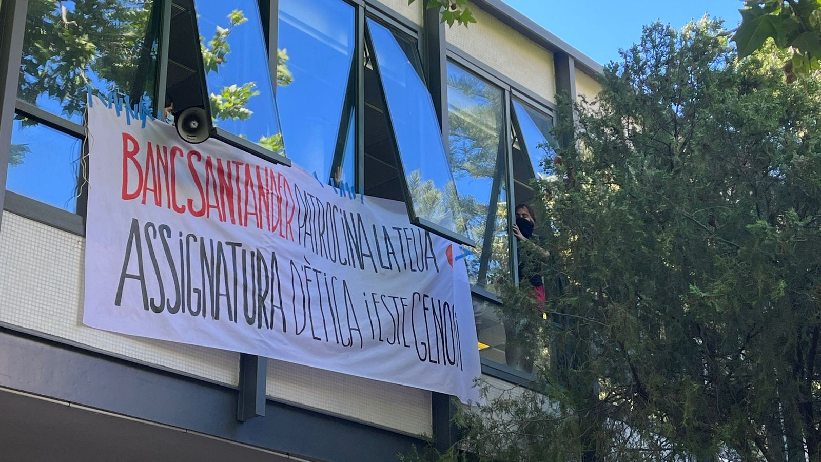 Pancarta en què es llig "Banc Santander patrocina la teua assignatura d'ètica i este genocidi"