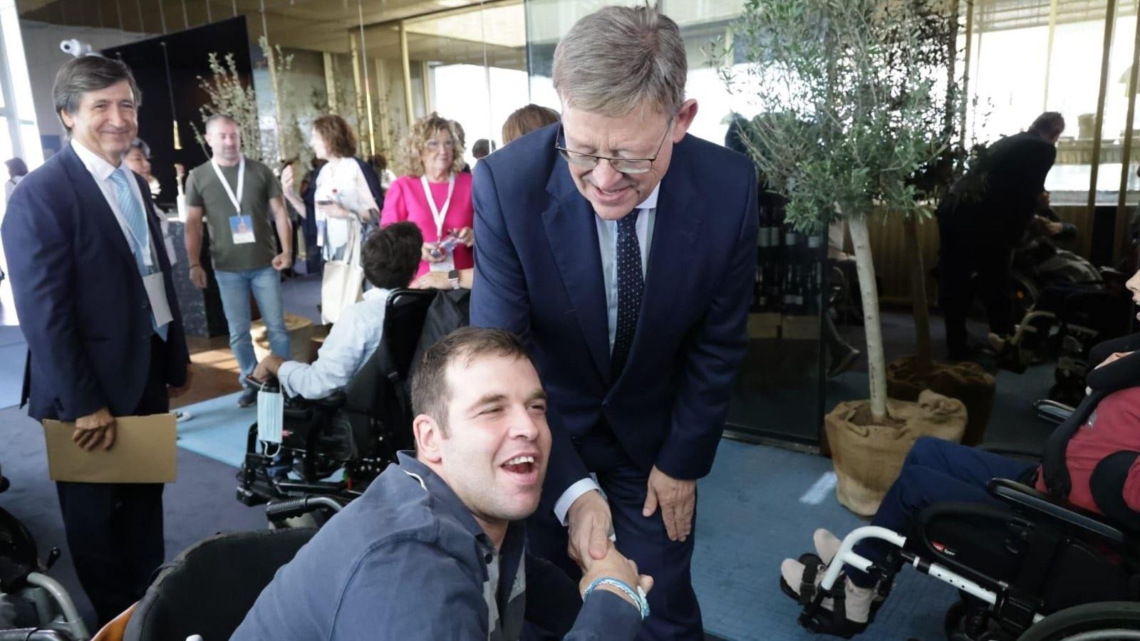 Una persona amb paràlisi cerebral saluda al president de la Generalitat Valenciana, Ximo Puig, a l'acte