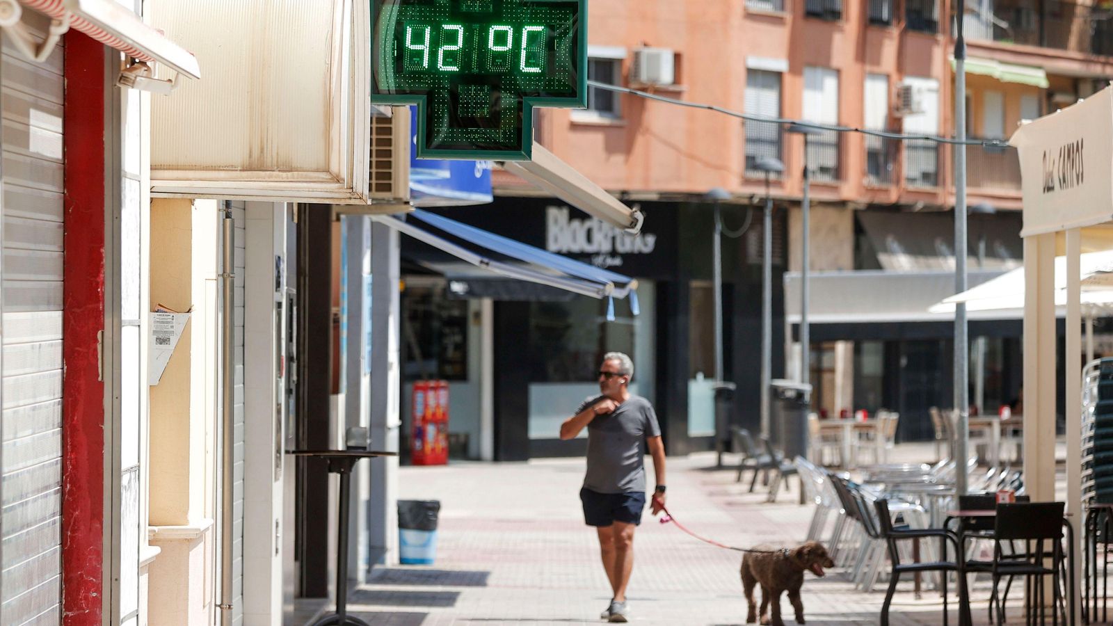 Un home passeja amb el seu gos davant un termòmetre urbà que marca 42 °C a Xàtiva