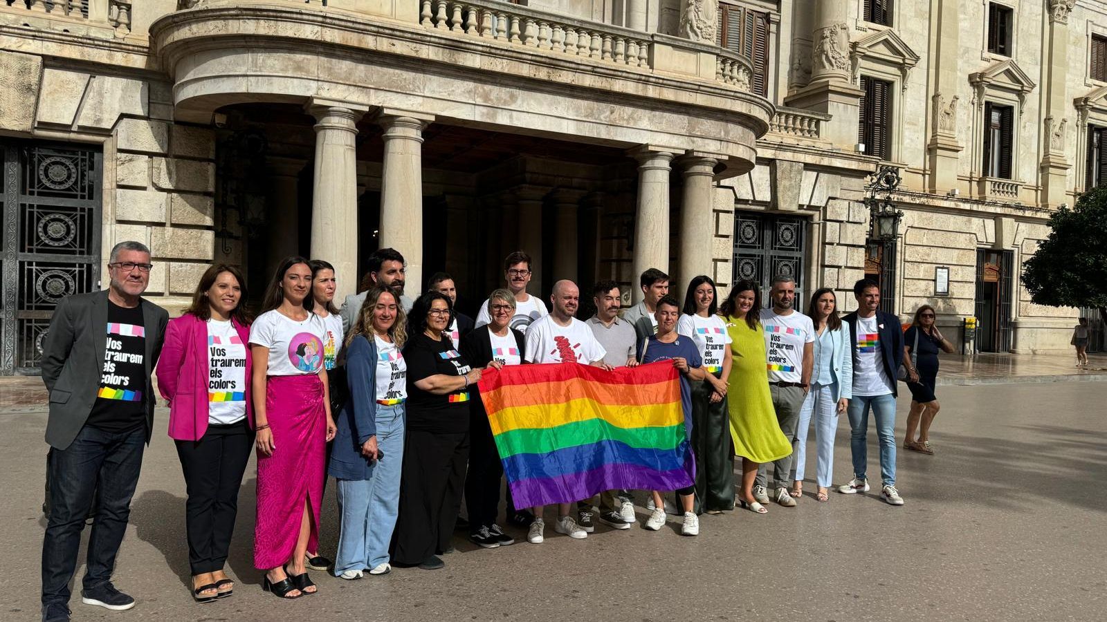 Els representants de Lambda amb polítics de Compromís i el PSPV exhibeixen la bandera LGTBI davant de l'Ajuntament de València