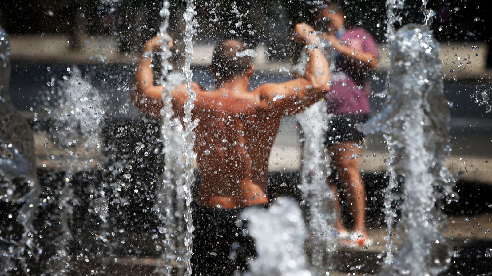 Un home travessa una font ornamental d'Alacant per a refrescarse