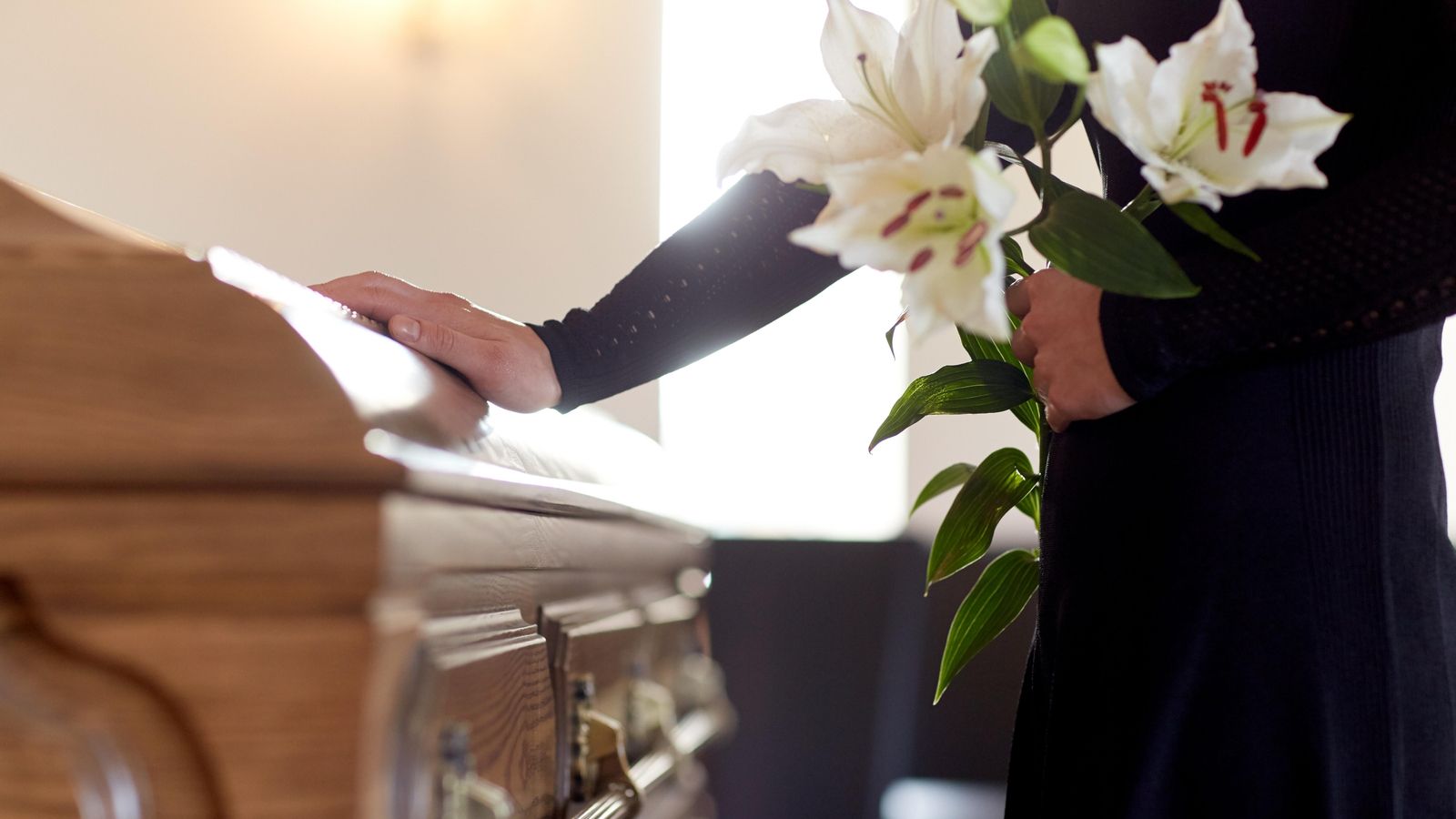Una dona amb flors de lliri blanc posa la seua mà en el taüt en un funeral a l'església