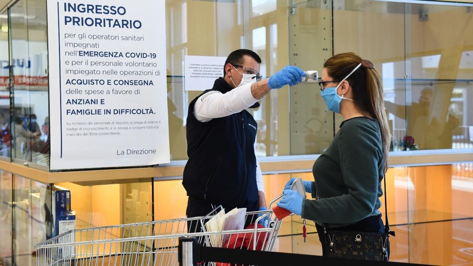 Un treballador comprova la temperatura d'una dona a l'entrada d'un supermercat de Torí, a Itàlia