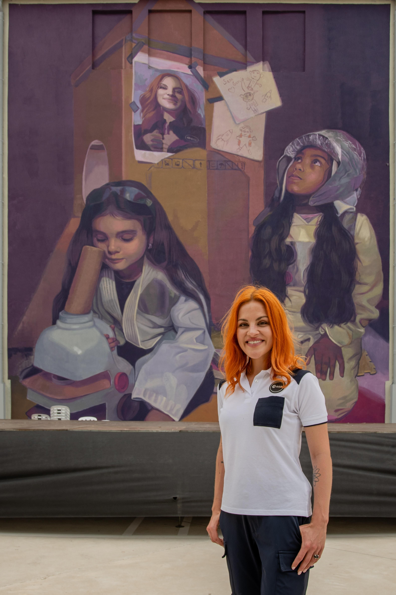 Sara García posant davant del seu mural el CEIP Cervantes de Gandia dins de la iniciativa Dones de Ciència