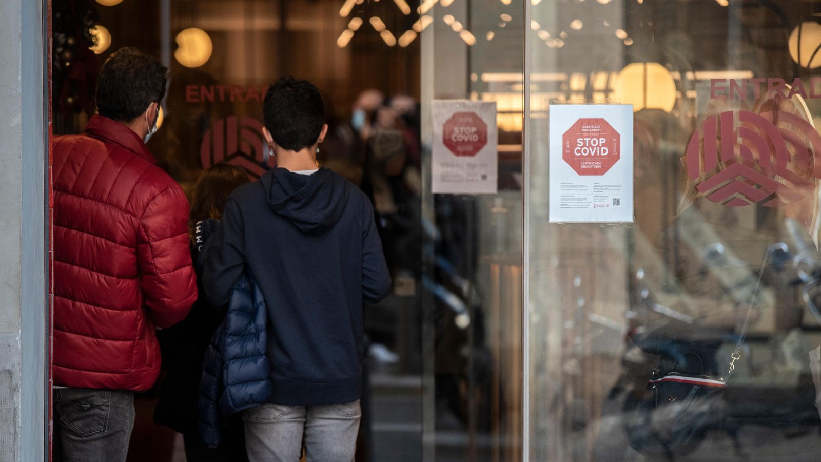 Dues persones entren a un restaurant de València amb un cartell que indica la necessitat d'acreditar la vacunació amb el passaport Covid