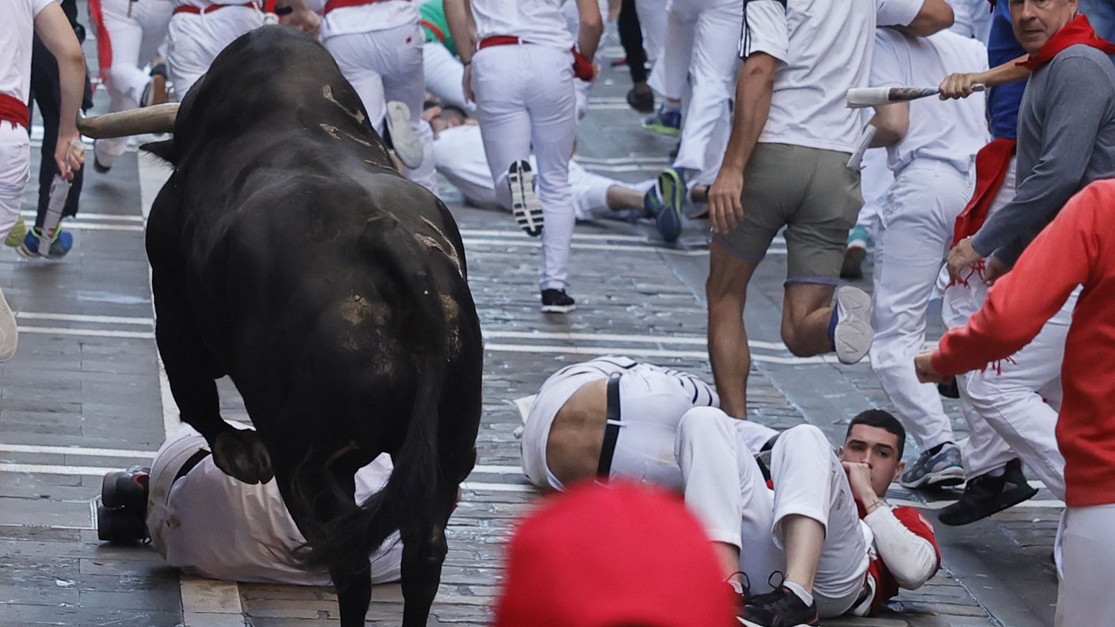 Diversos mossos cauen davant un bou ressagat en el tram inicial del carrer de l'Estafeta durant el segon 'encierro'