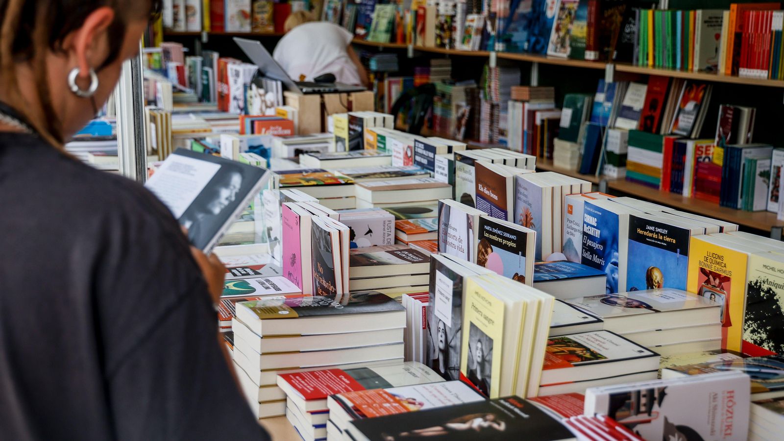 Una jove observa la portada d'un llibre en la Fira del Llibre de València