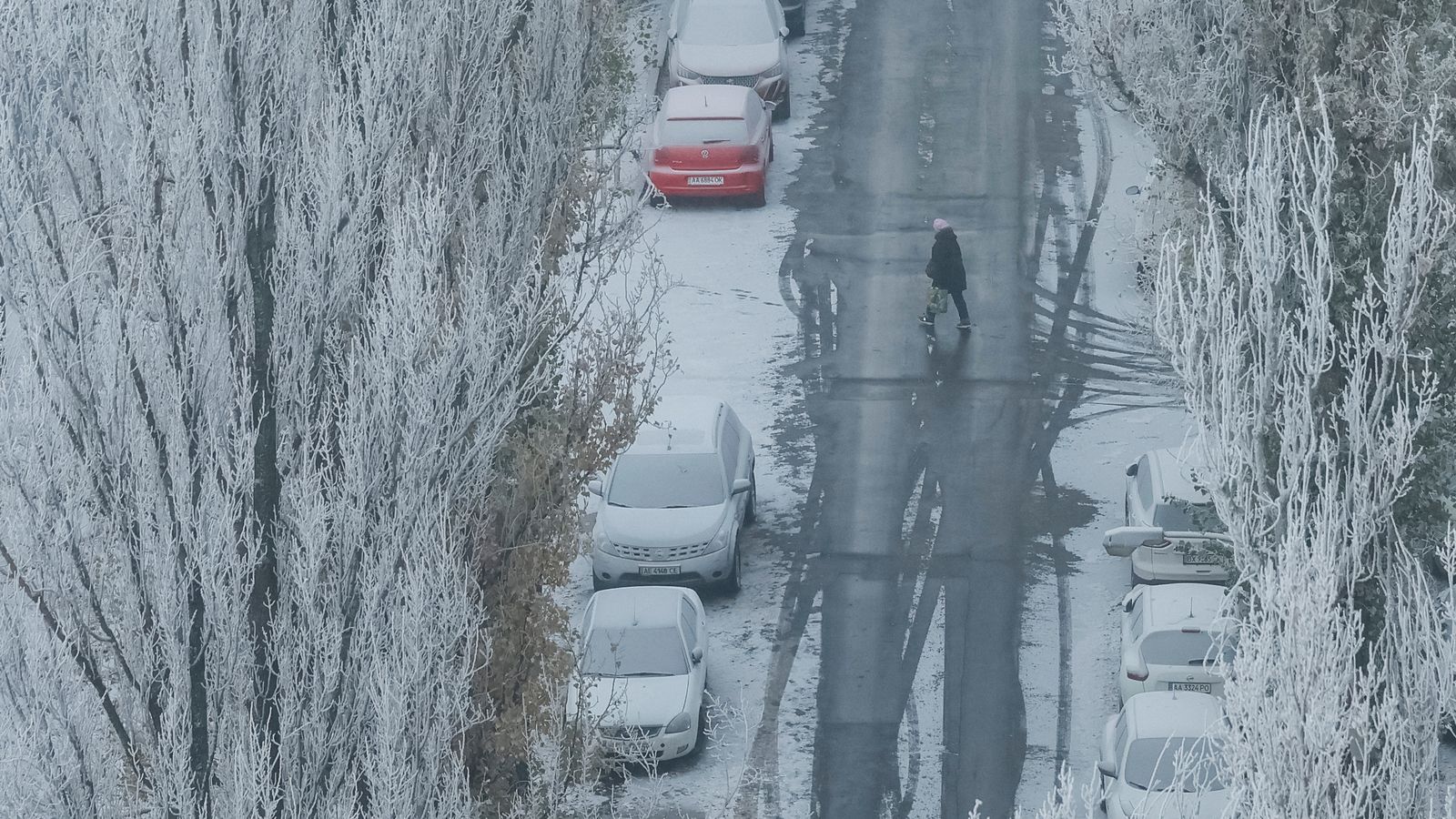 Una dona travessa el carrer a Kíiv entre arbres coberts de neu en un matí gelat, enmig de l'atac de Rússia a Ucraïna