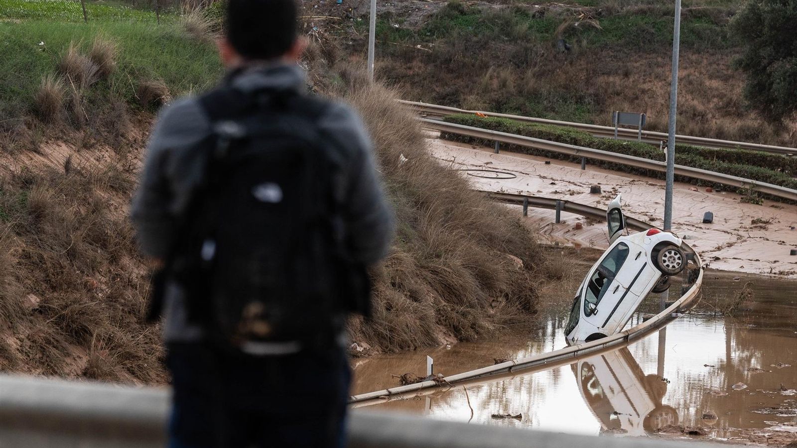 Un jove amb una motxilla, al costat d'una carretera destruïda per la DANA