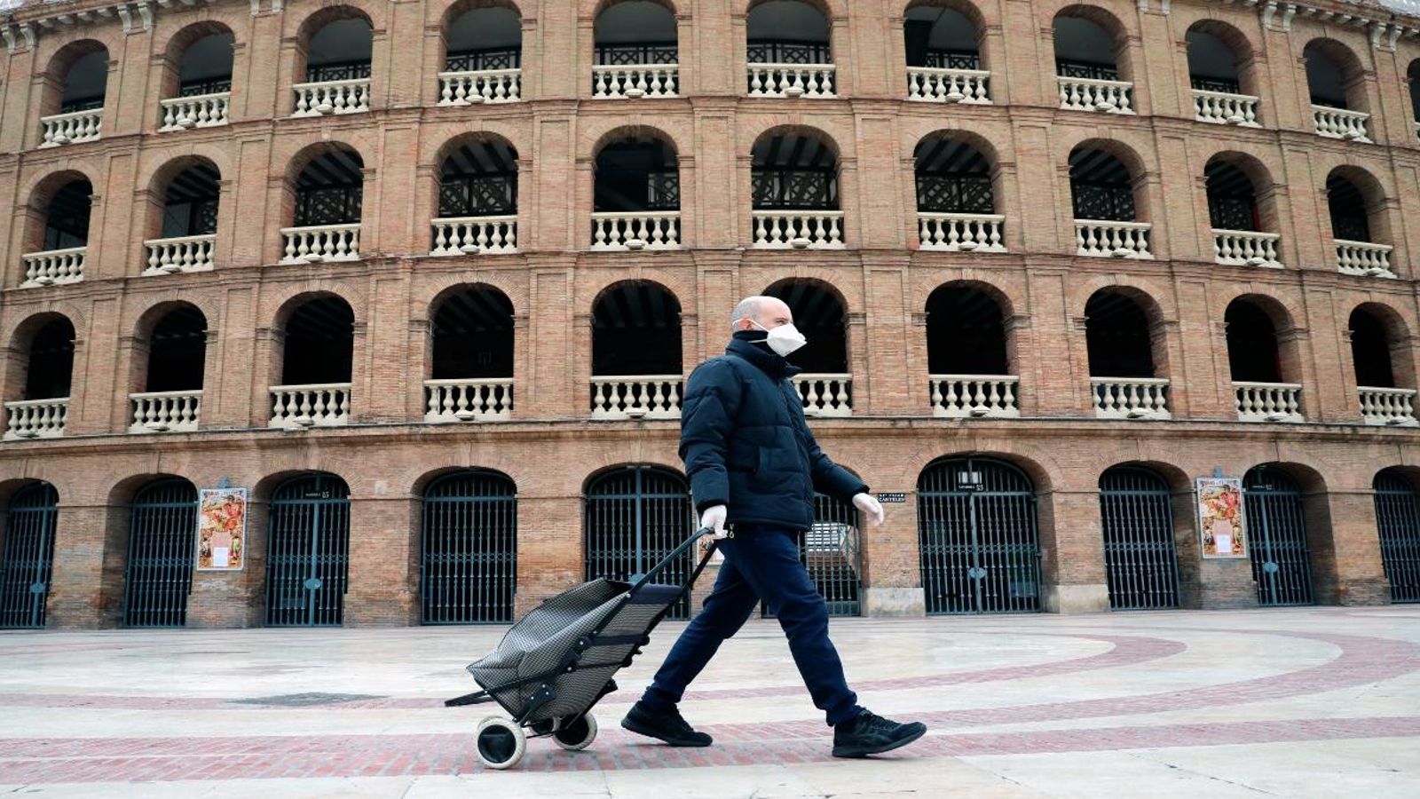 Un vianant protegit amb mascareta i guants passa per davant de la plaça de bous de València
