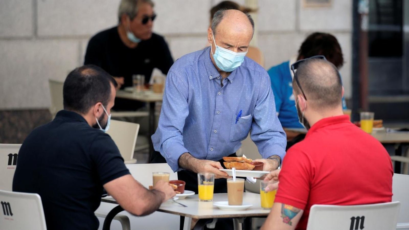 Un cambrer serveix el desdejuni a dos homes asseguts en la terrassa d'un bar