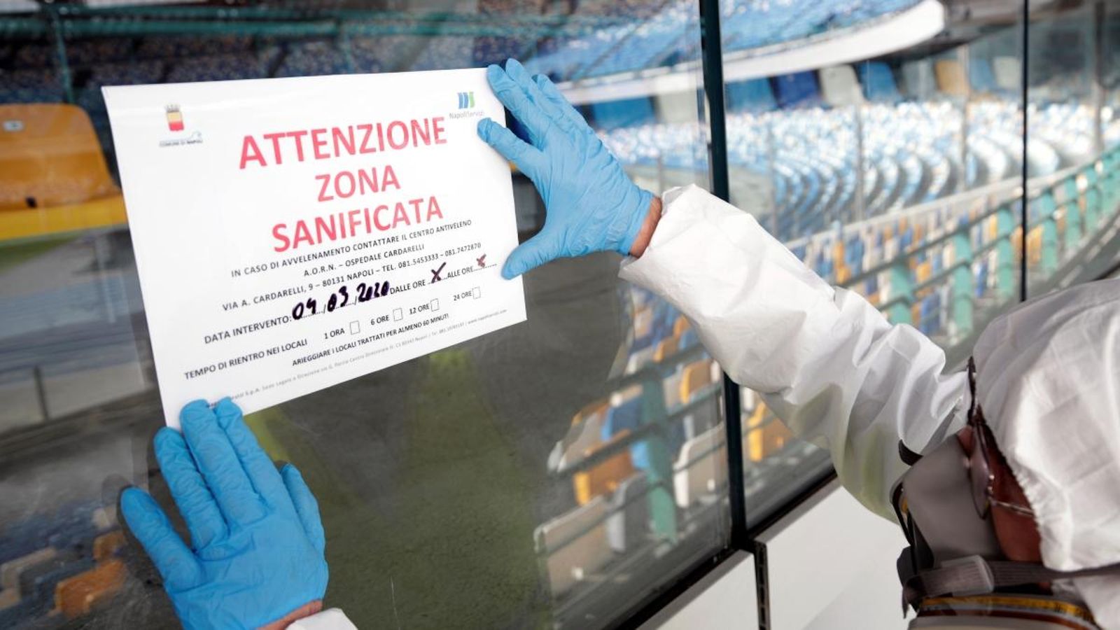 Un netejador que porta vestit de protecció ajusta un cartell que diu "Atenció: aquesta zona ha estat sanejada" a l'estadi de San Paolo de Nàpols
