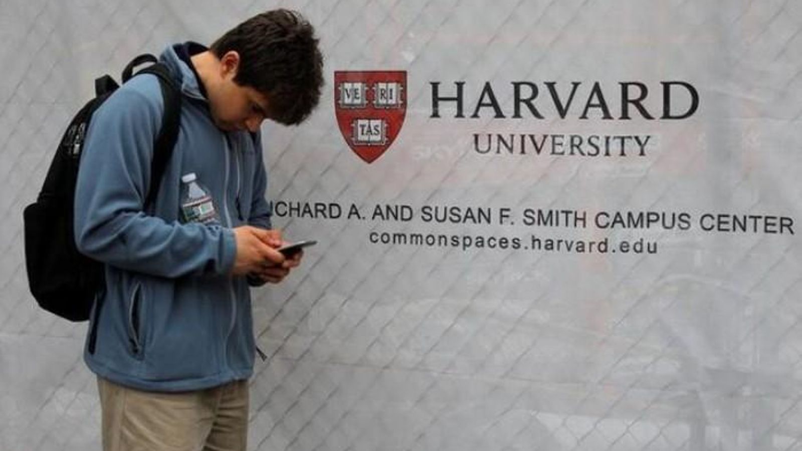 Un estudiant mira el seu telèfon mòbil al costat d'un cartell de la Universitat d'Harvard a Cambridge, Massachusetts, els EUA