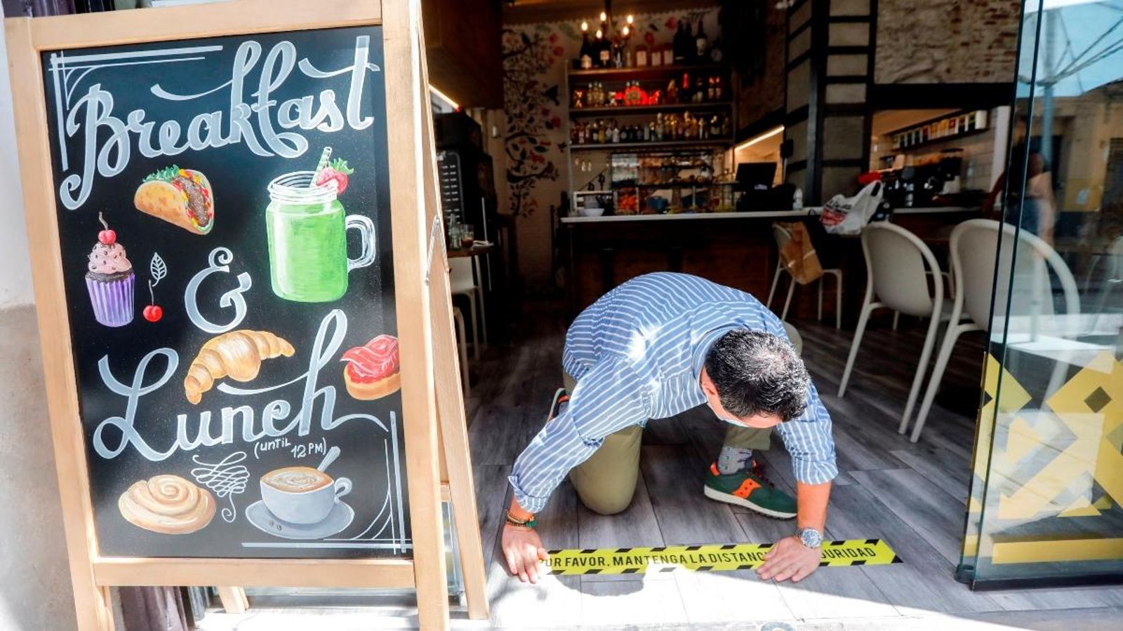 Un home enganxa un cartell amb el lema "Per favor, mantinguen la distància de seguretat" a l'entrada d'un bar a la Comunitat Valenciana