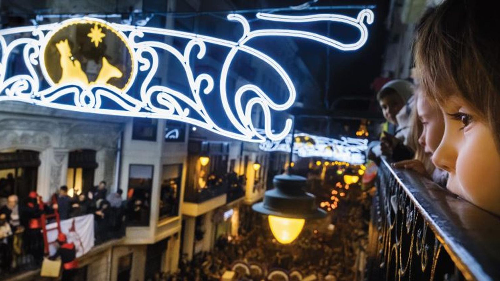 Diversos xiquets i xiquetes miren des del balcó de sa casa com avança la cavalcada dels Reis d'Orient pels carrers d'Alcoi