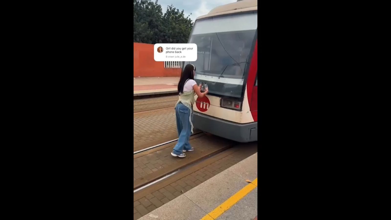 Una jove col·loca el mòbil en la part posterior d'un vagó per a córrer darrere quan arranque la marxa