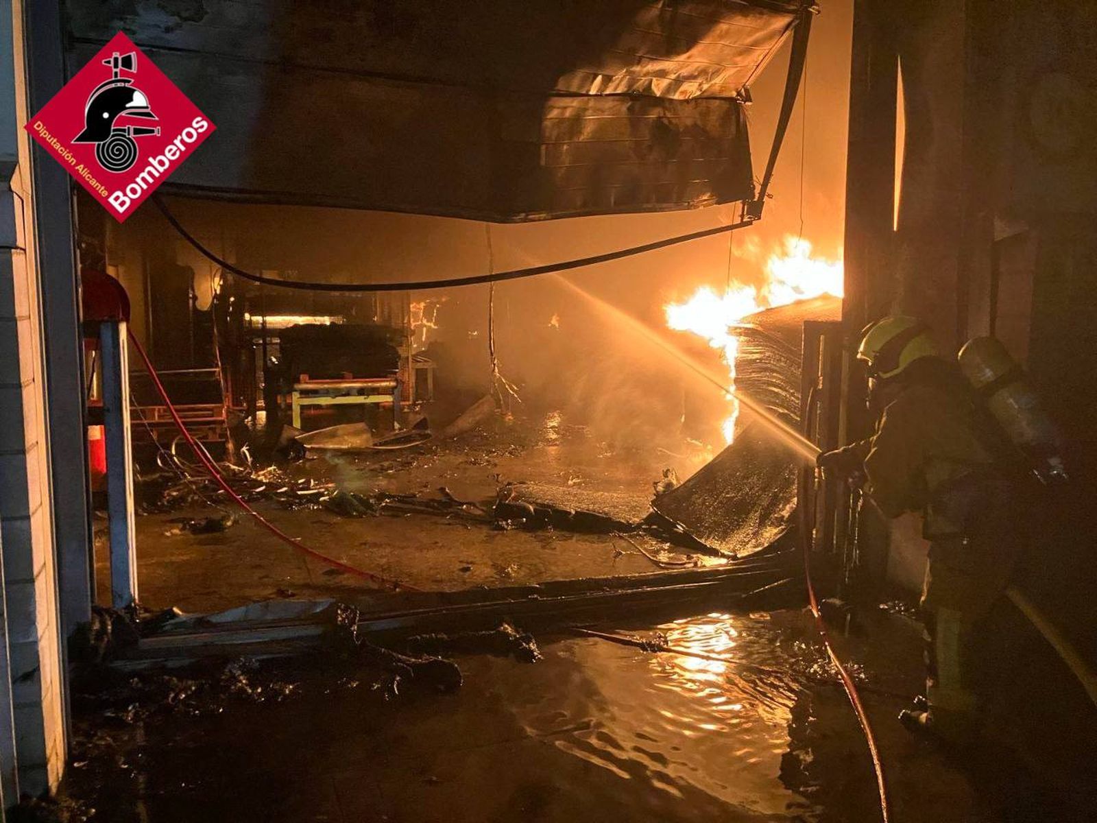 Un bomber tracta, des de fora de la nau industrial, de rebaixar les flames que es van estendre ràpidament per l'interior de la fàbrica de calcer