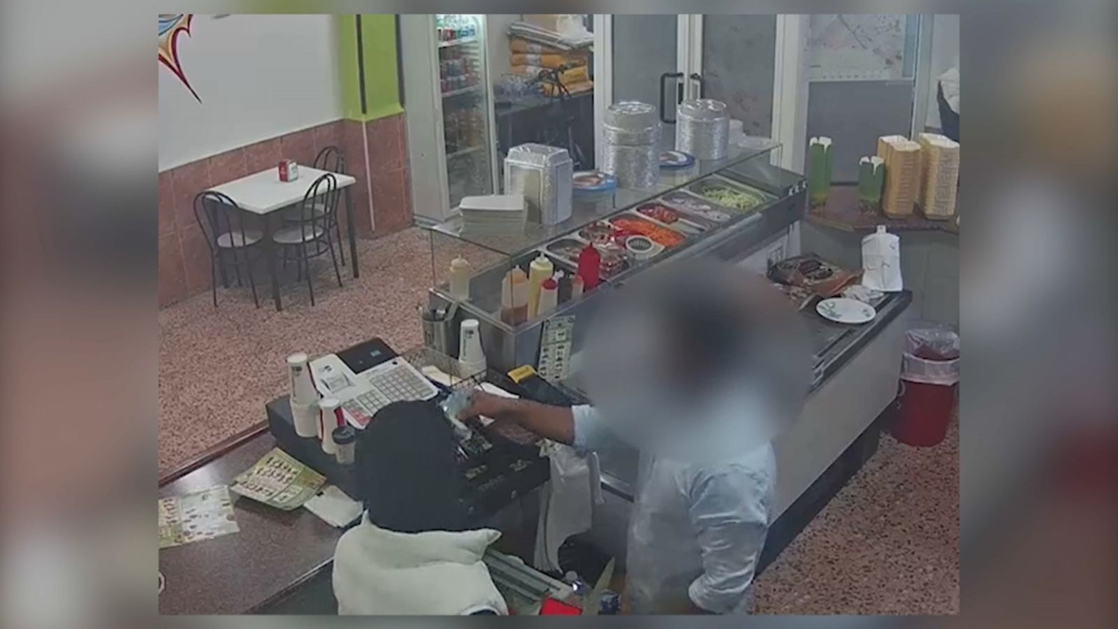 Un dels lladres amenaça el propietari d'un comerç per a furtar els diners de la caixa