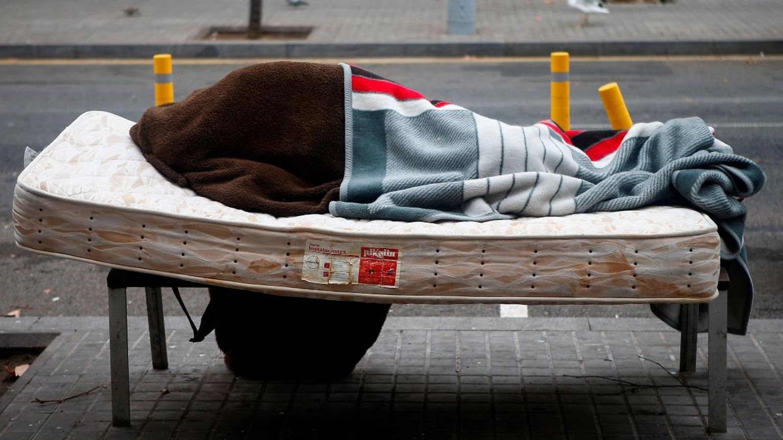 Una persona sense llar descansa sobre un banc del barri de Sant Andreu de Barcelona, en una imatge del divendres