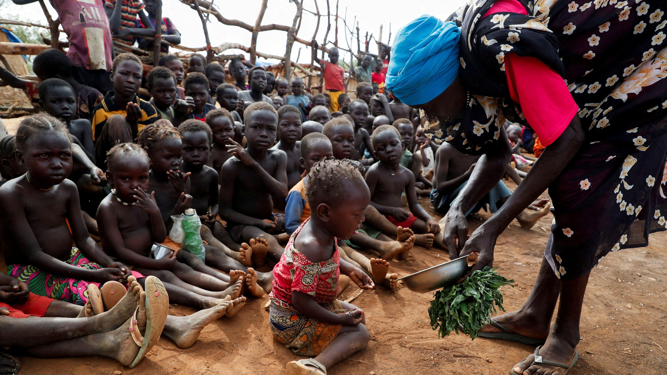 Una dona desplaçada serveix fulles bollides per a menjar a xiquets orfes en un campament del Sudan Una dona desplaçada serveix fulles bollides per a menjar a xiquets orfes en un campament del Sudan