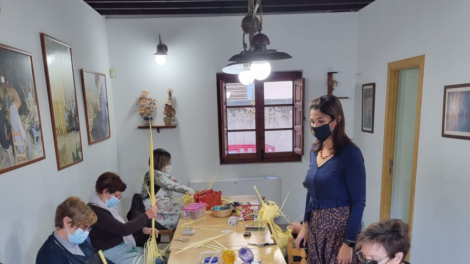 La regidora de Cultura d'Elx, Marga Antón, visita un taller on un grapat de dones estan teixint palmes