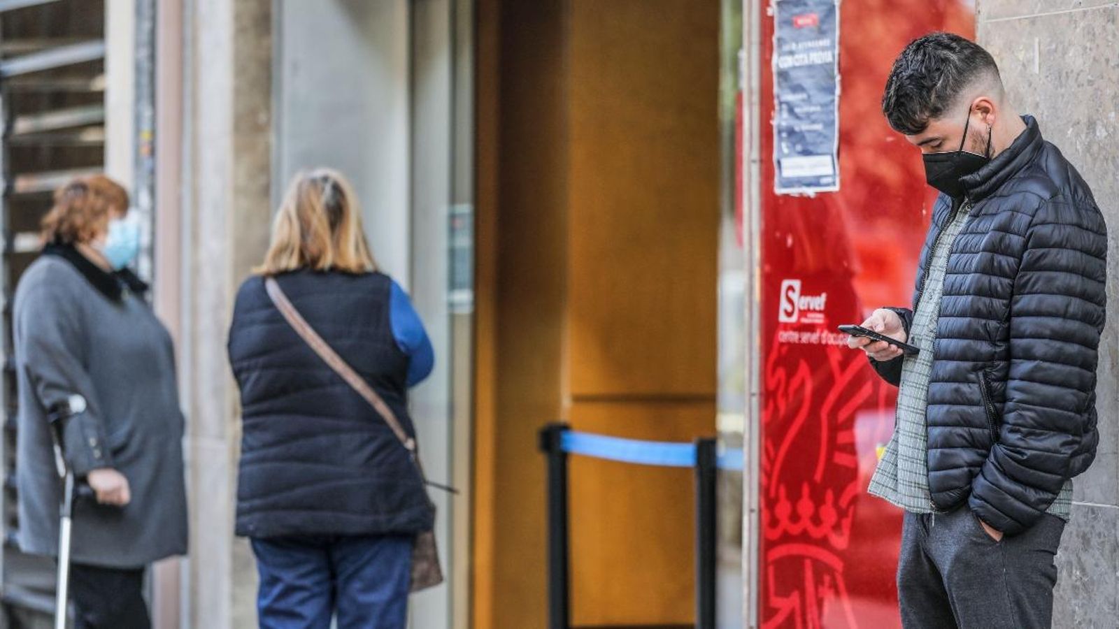 Un jove mira el telèfon mentre espera per a entrar en una oficina del Sepe a València
