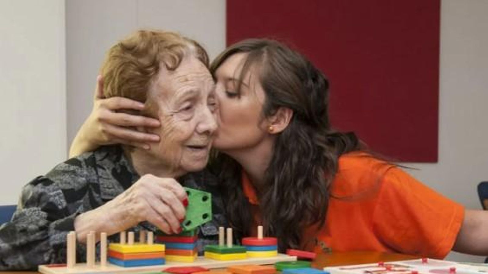 Una cuidadora dona un bes a una dona major