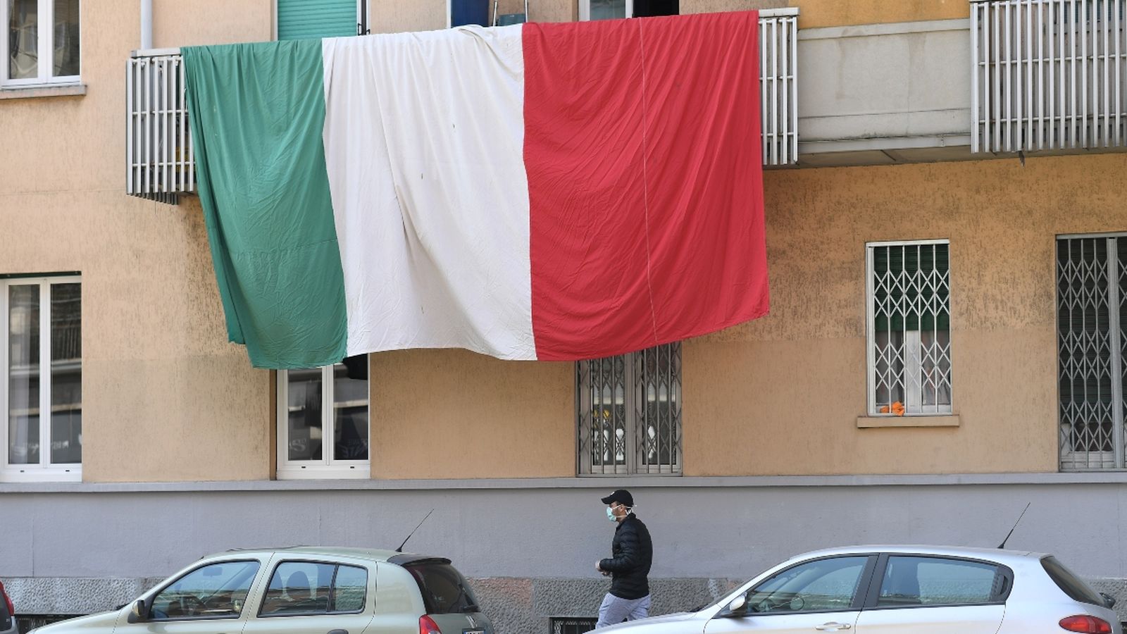 Un home passeja sota una bandera italiana penjada des d'un balcó, a Milà