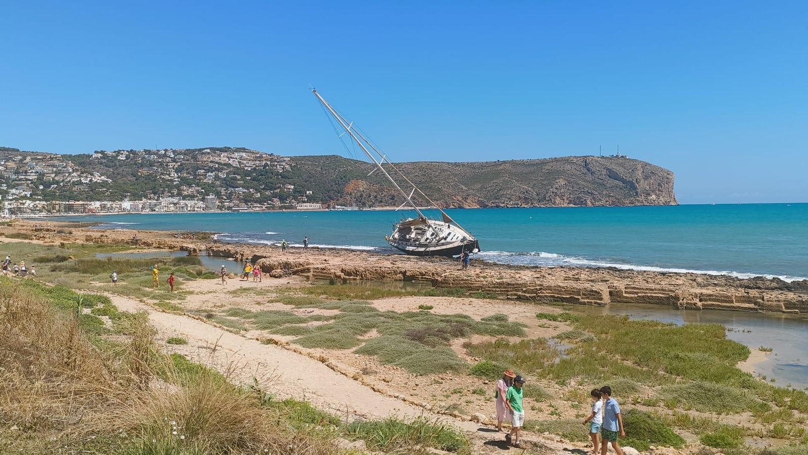 El veler continua encallat entre les roques de la platja Primer Muntanyar, davant la mirada de banyistes i curiosos que s’apropen