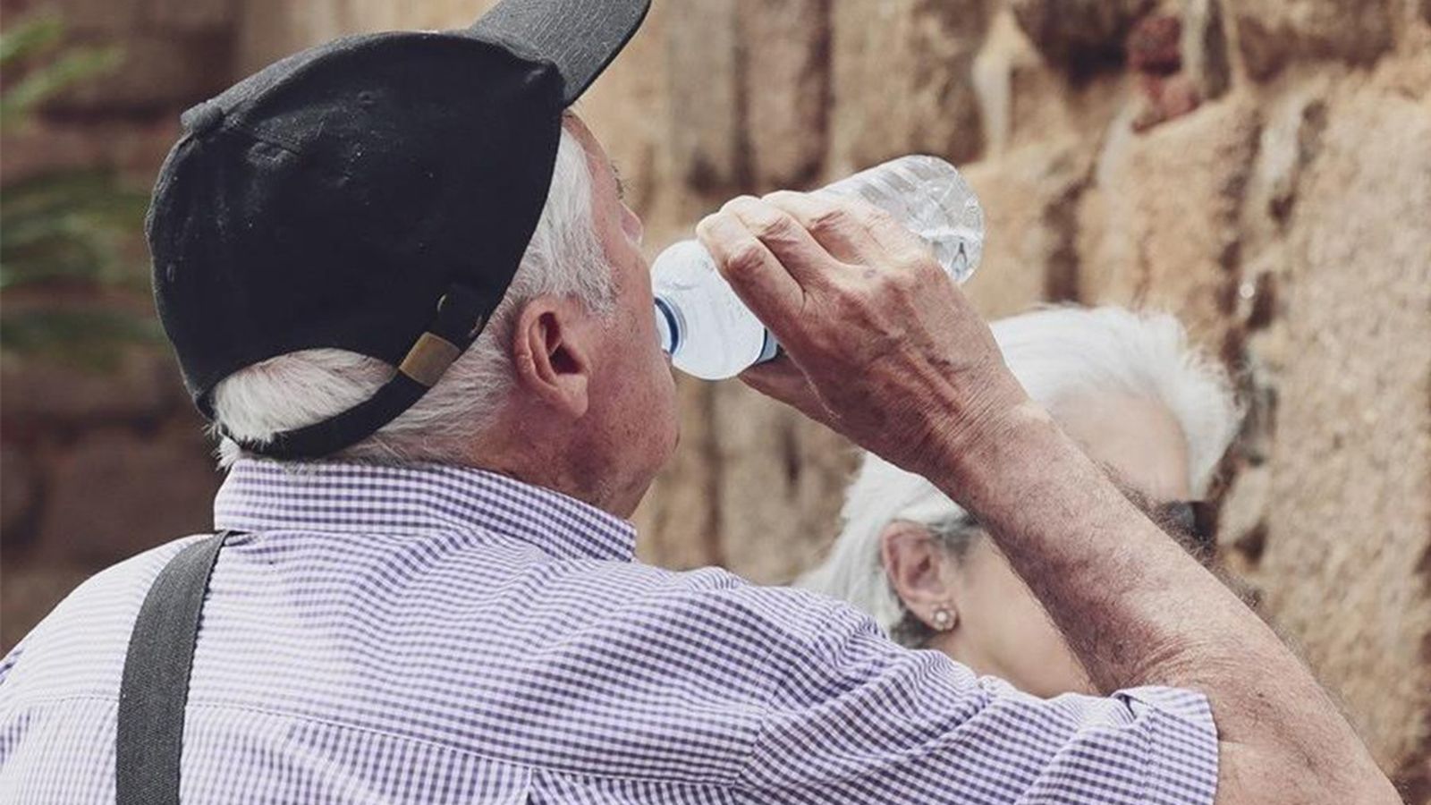 Un home gran beu aigua per a combatre la calor i la deshidratació