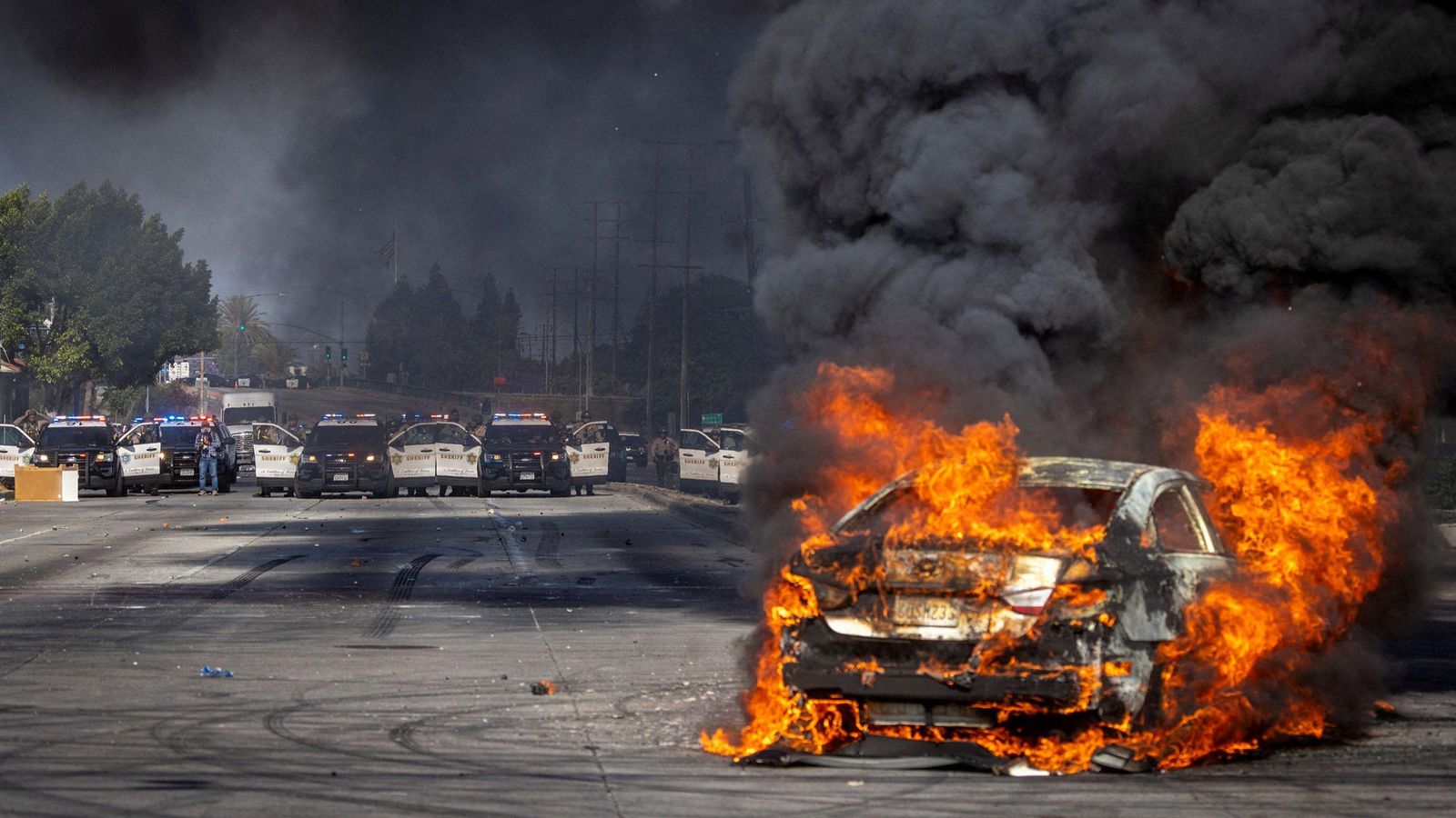 Un vehicle en flames davant un operatiu policial a Los Angeles, en el marc de les protestes contra les batudes per a caçar migrants sense papers