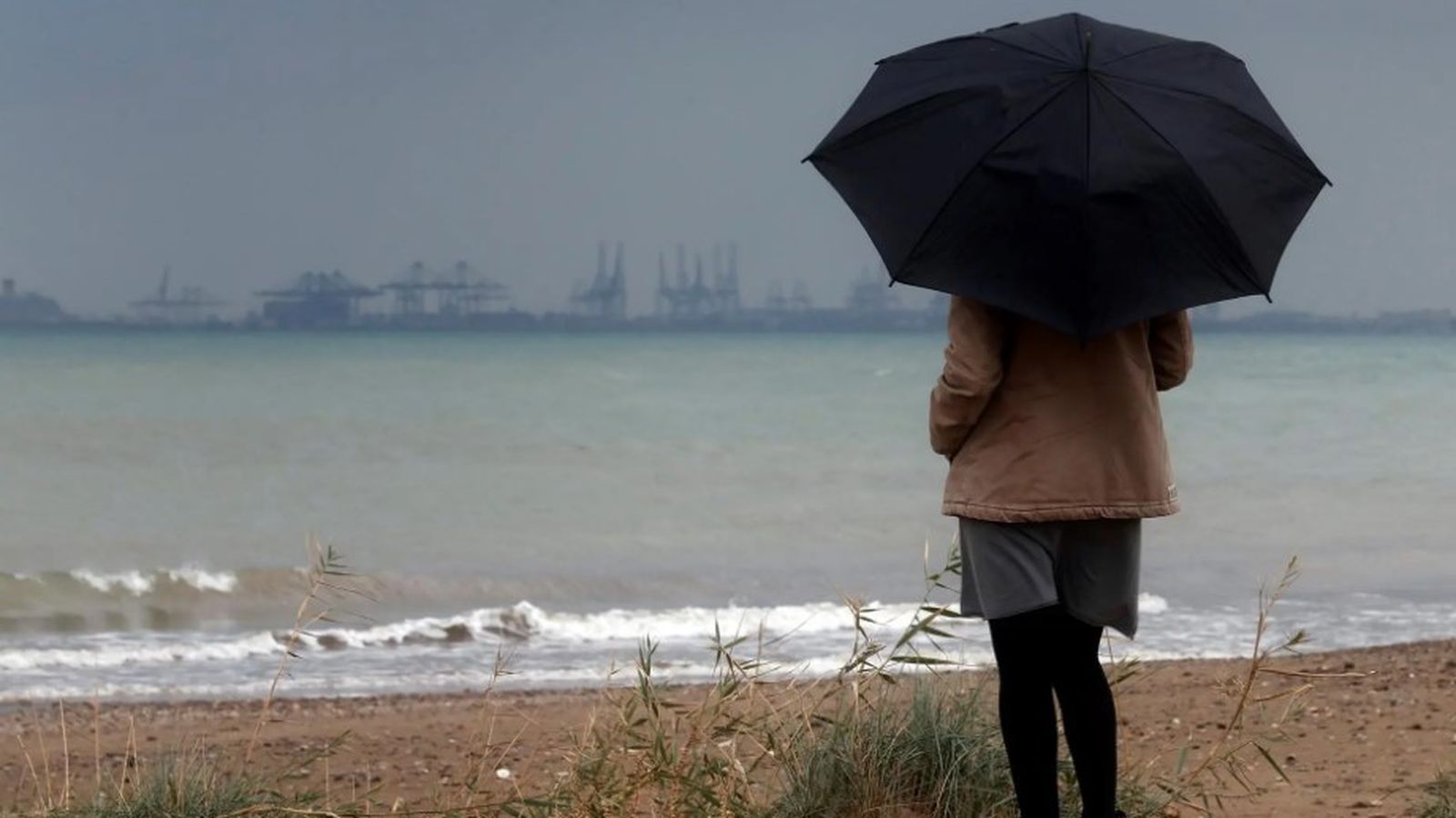Una dona amb un paraigua enfront del port de València en una imatge d'arxiu