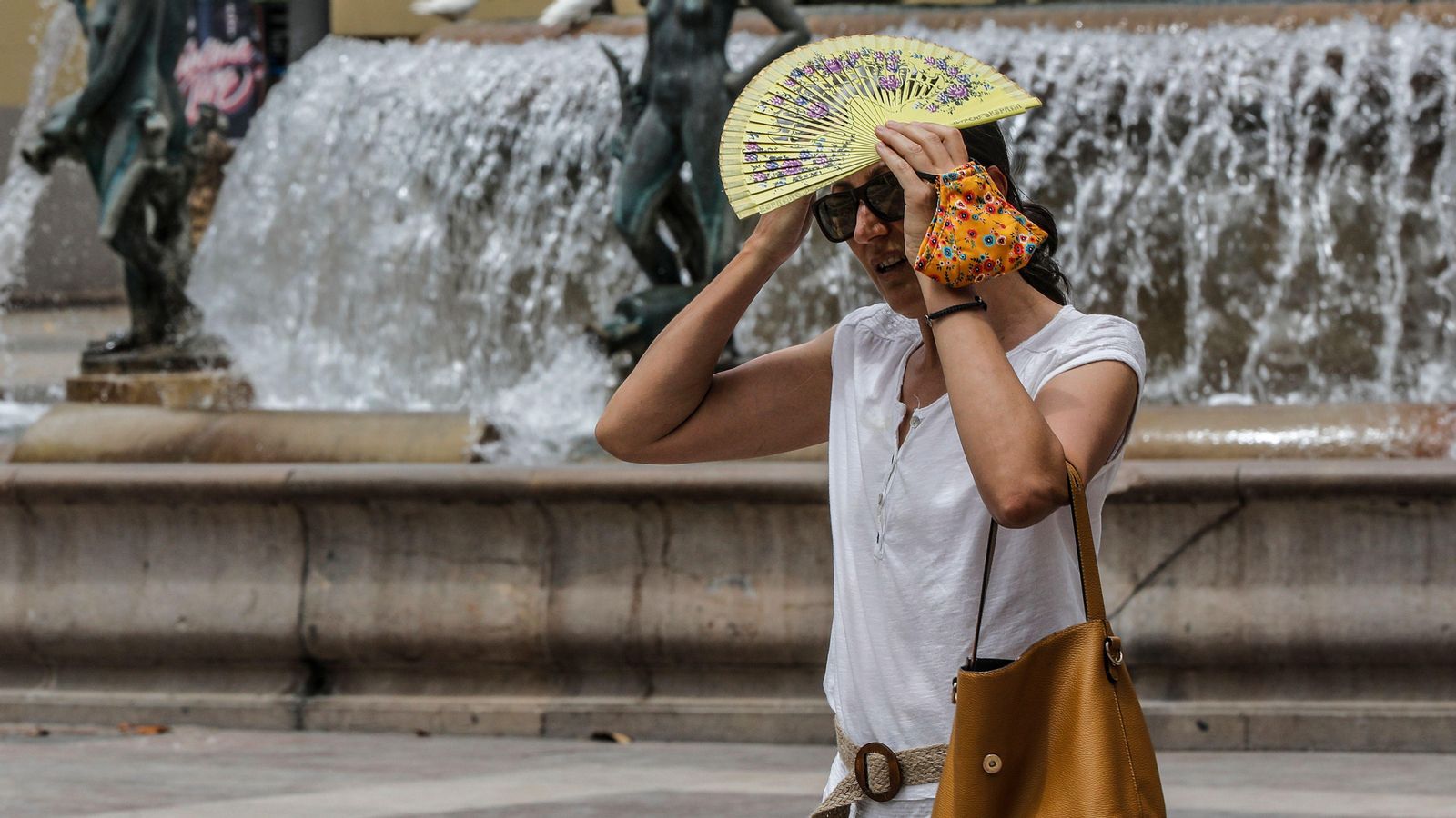 Una dona es tapa el cap amb un ventall per a protegir-se de les altes temperatures