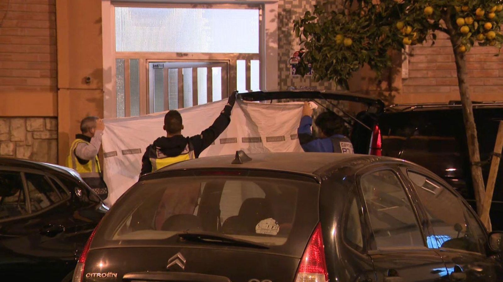 Agents de policia tapen amb un llançol la porta de l'edifici on van trobar morta la dona