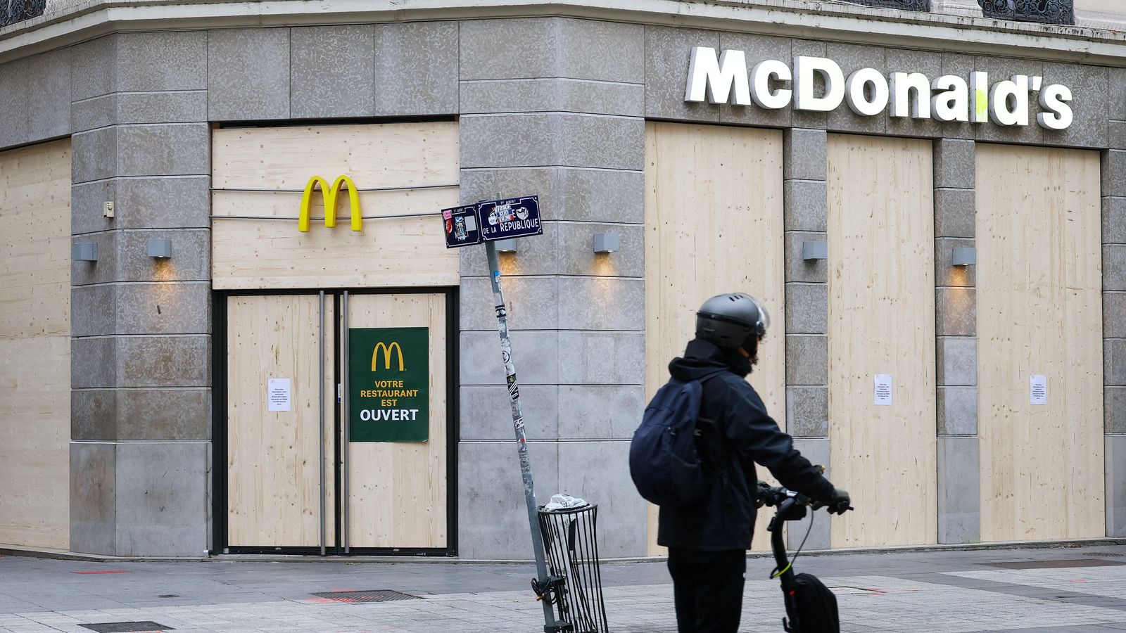Una persona circula amb patinet davant d’un McDonald’s amb els aparadors protegits amb taulons de fusta este dissabte.